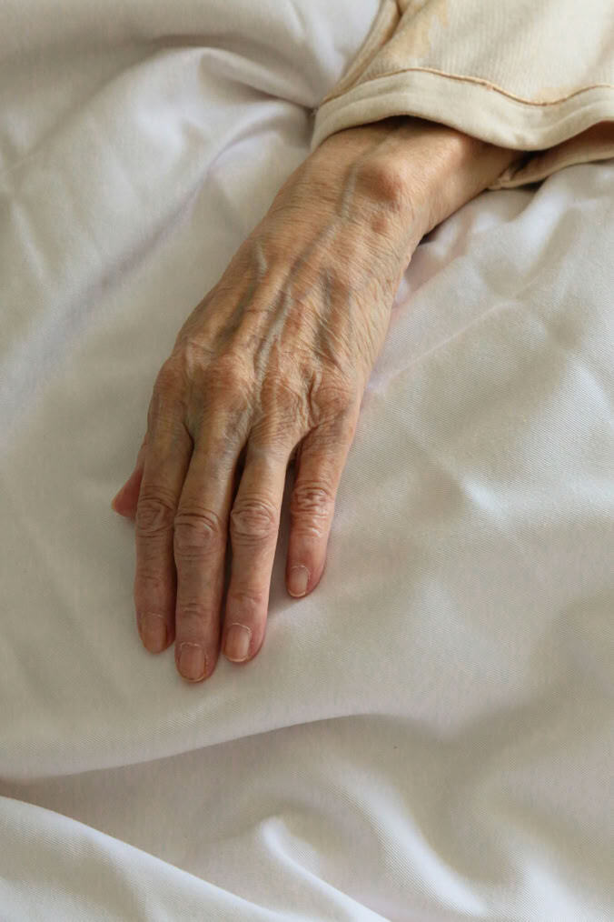An elderly hand resting on a white sheet