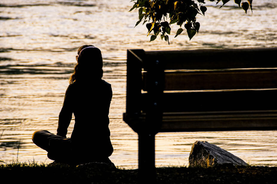 A person sitting in meditation by the water at sunset